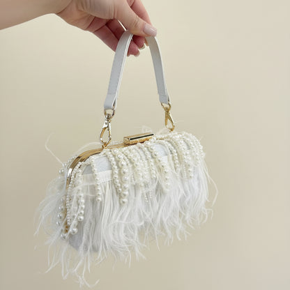 A white handbag with feather embellishments and a pearl detail, held in a person's hand.