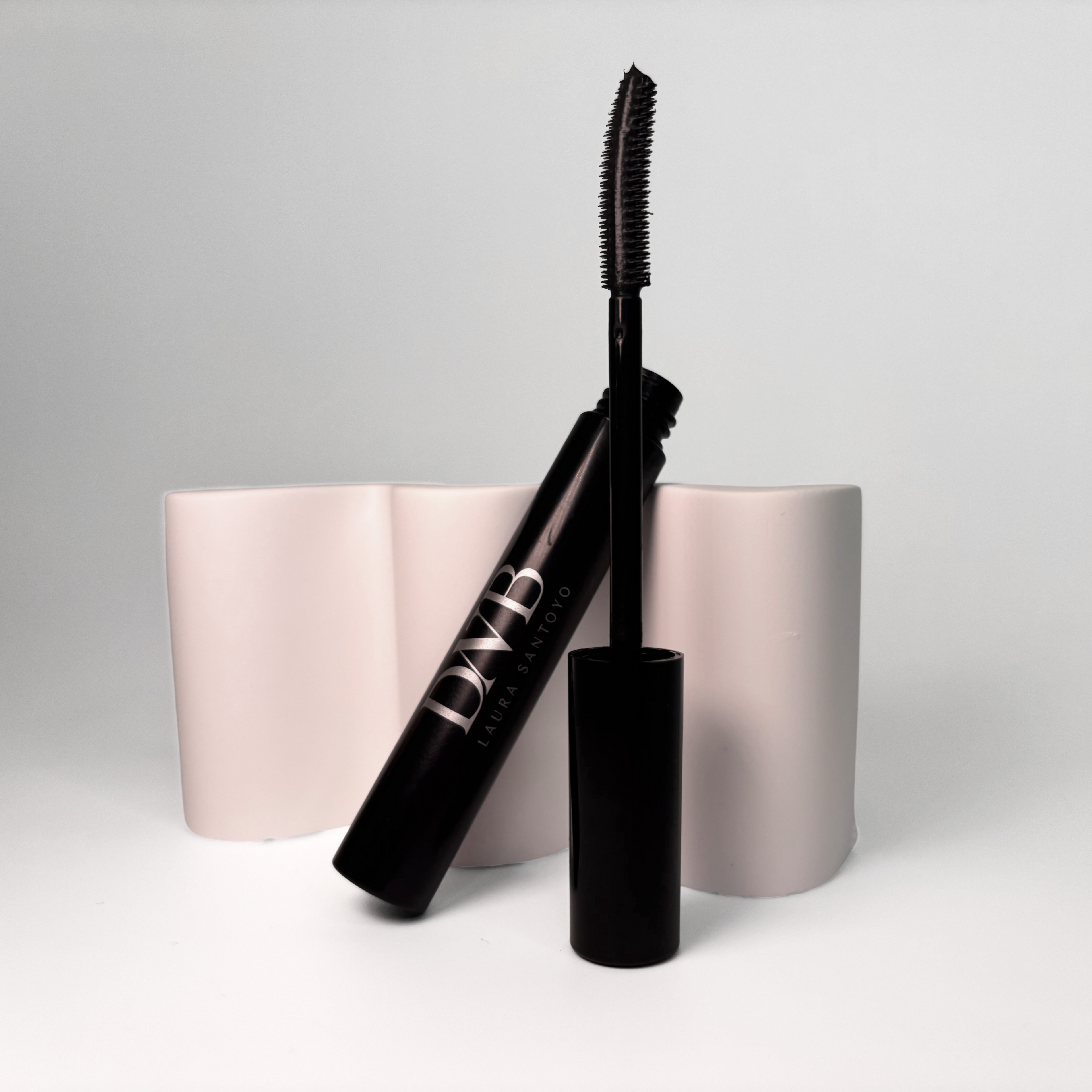 Black mascara with a white cylindrical holder on a light gray background