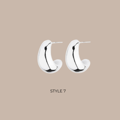A pair of polished silver crescent-shaped hoop earrings displayed on a solid beige background with the text 'STYLE 7' underneath.